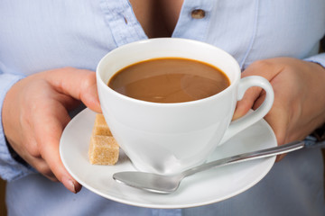 Hand holds mug of coffee with milk with spoon and brown sugar
