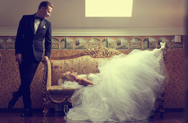 Beautiful bride on a sofa and groom near her in a luxury hotel