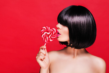 young girl in black wig holding lollipop and posing for camera