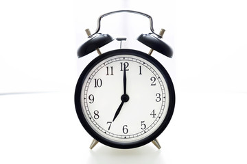 Oldfashioned black glossy alarm clock showing 7 o'clock