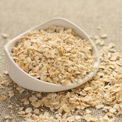 Oat flakes in white ceramic bowl on sackcloth background