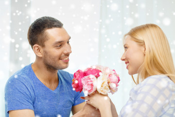 smiling man giving girlfriend flowers at home