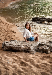 sexy woman sitting on big rock at sandy sea shore