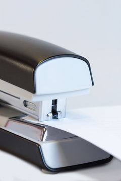 Closeup of a grey office stapler stapling white paper