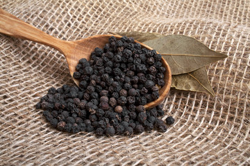 Black pepper in wooden spoon with dry bay leaves on burlap backg