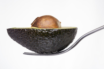 half of an avocado laying on a fork, isolated on white