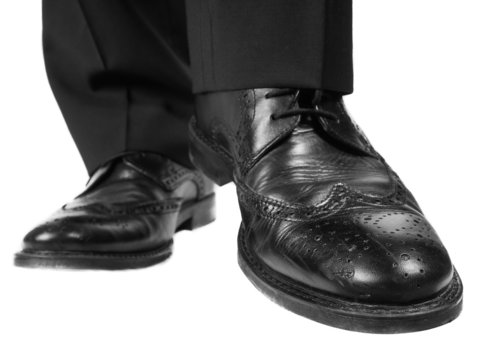 Person in black suit and shoes lifting one foot towards white