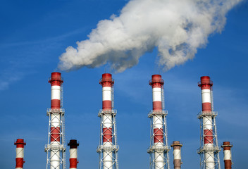 Manu industrial pipes with white smoke over blue sky