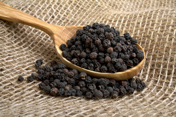 Black pepper in wooden spoon on burlap background