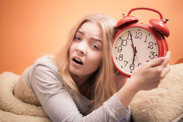 Unhappy girl in bed with alarm clock