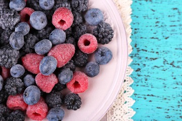 Iced berries on plate, on color wooden background