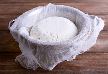 Cottage cheese on gauze in colander on wooden background