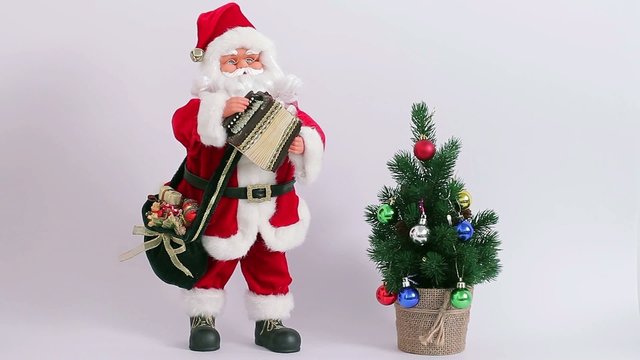 Santa playing the accordion near a Christmas tree