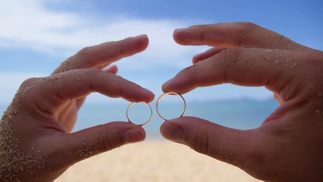 Wedding Rings in Hands on Beach against Sea.