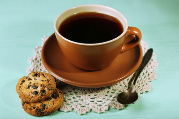 Glass cup of coffee and tasty cookie on color wooden background