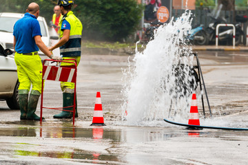 road spurt water beside traffic cones and two technicians