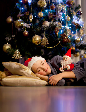 A boy sleeps under the Christmas tree 