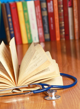 A stethoscope is lying with a book on the desk against books.