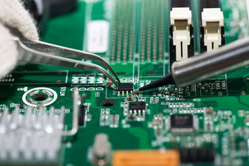 Electronic component held with tweezers on motherboard