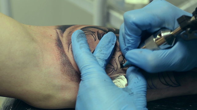 Tattoo artist working. Man draws on his arm woman's face.