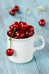 white mug of fresh cherries on blue wooden table