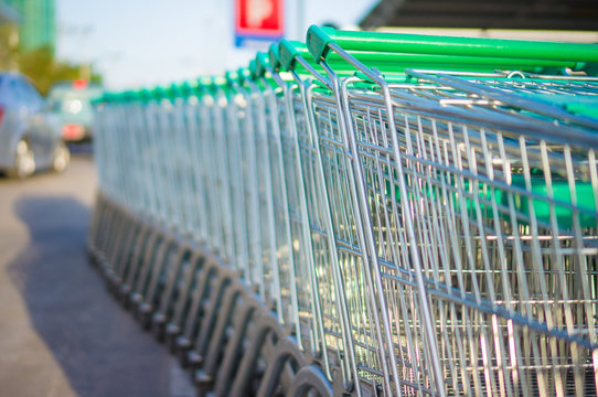 Row of shopping cart with green handles on parking near supermar