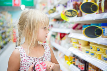 Adorable girl sit with set of good in shopping cart in supermark