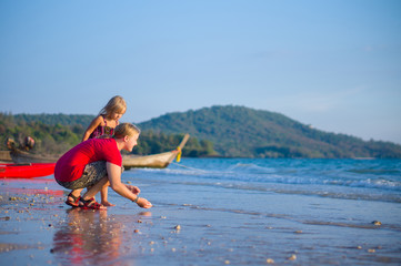Mother and daughter collect sea shells on the beach