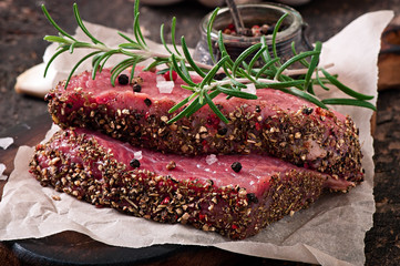 Raw beef steak with spices and a sprig of rosemary