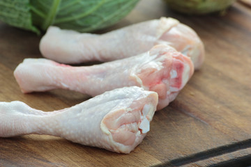 Three chicken drum sticks on a wooden chopping board.