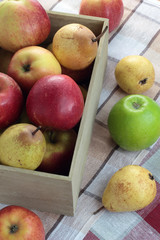 Loose apples and pears next to a box full of fruit.