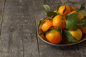 tangerines with green leaves on a tray on a wooden background