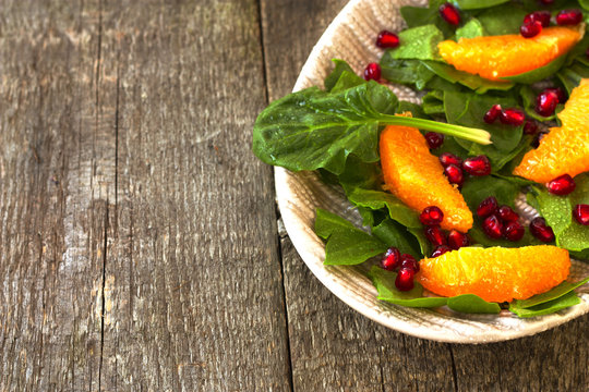 spinach salad, orange and pomegranate on a wooden background