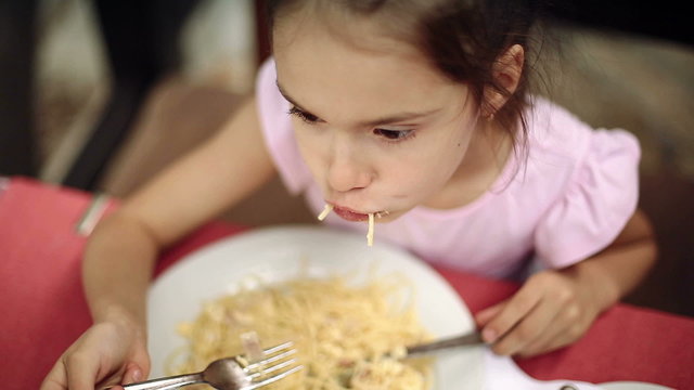 Child eats spaghetti pasta in the restaurant near the sea