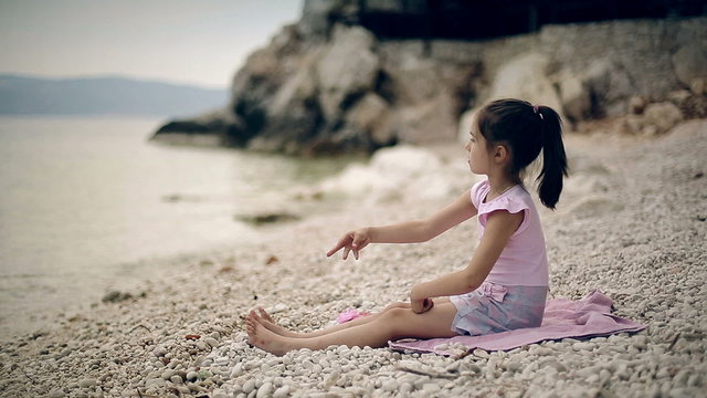 Child sits on the beach and throwing stones into the water.