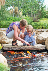 Woman and daughter feeding fishes in pond.