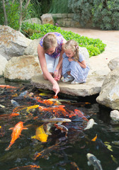 Woman and daughter feeding fishes in pond.