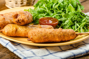 Corn dog with fresh arugula salad and hot dip