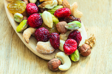 Varieties of dried fruits and nuts on wooden spoon.