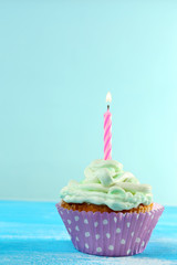 Delicious birthday cupcake on table on light blue background