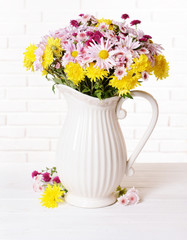 Beautiful flowers in pitcher on table on light background