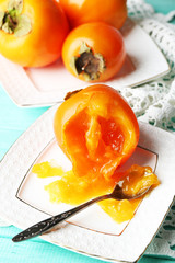 Ripe persimmons on plate, on wooden background