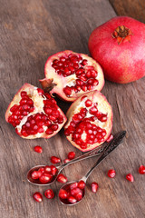 Juicy ripe pomegranates seeds in spoons, on old wooden table