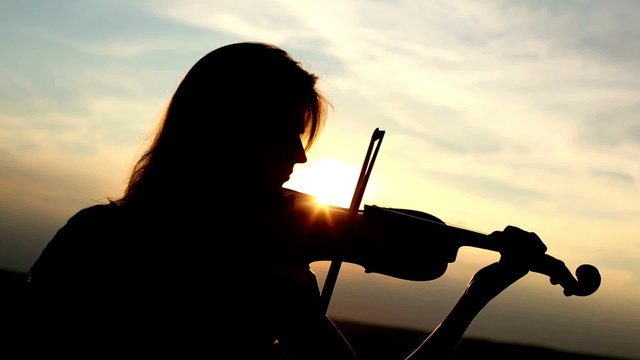 Silhouette girl violinist playing the violin at sunset sky.
