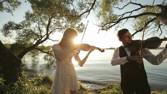 Violin duet man and woman play violin on nature at the sunset.