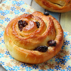 Obraz na płótnie Canvas Fresh sweet swirl buns with raisins on colored wooden table
