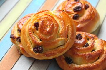 Fresh sweet swirl buns with raisins on colored wooden table