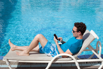 young man using smartphone near the pool in luxury hotel