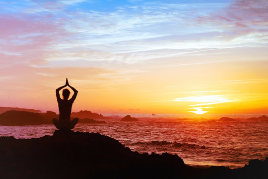 woman meditating at sunset, silhouette of person practicing yoga