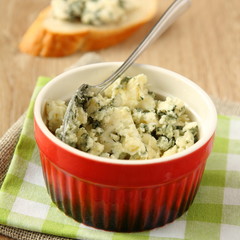 Blue cheese in red bowl on wooden background